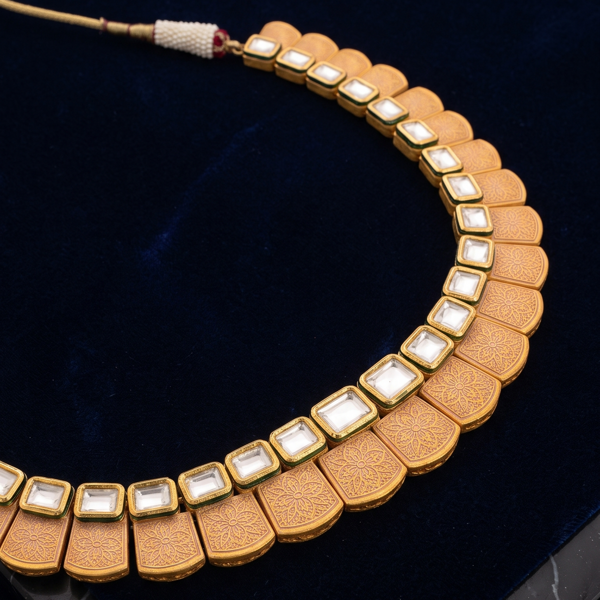 A gold-toned statement necklace with scalloped segments set with white stones, displayed on a dark blue velvet surface.