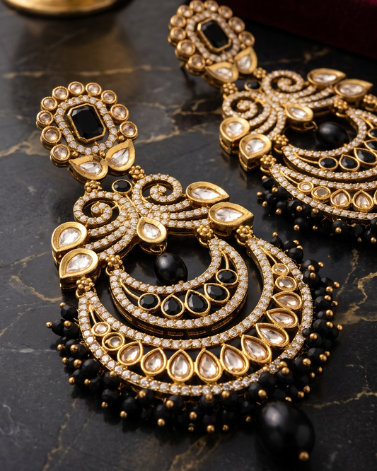 Gold-toned traditional Indian earrings with black stones, clear crystal-like stones, and black bead fringe, displayed on a dark marble surface with a red jewelry box in the background.