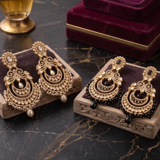 Two pairs of ornate gold-toned traditional dangle earrings displayed on carved wooden trays, with a dark purple velvet jewelry box and a perfume bottle in the background on a black marble surface.