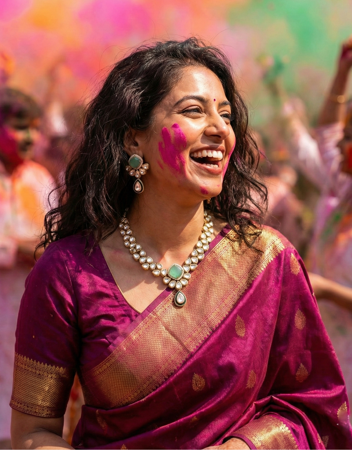 A woman wearing a magenta purple and gold saree smiles joyfully outdoors during a Holi festival, with colorful powder in the air behind her.