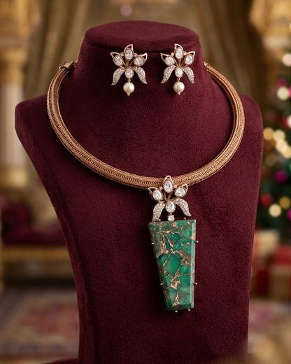 A luxury jewelry set displayed on a dark burgundy velvet mannequin bust, featuring a gold-tone chain necklace with a large green stone pendant and matching flower-shaped stud earrings.